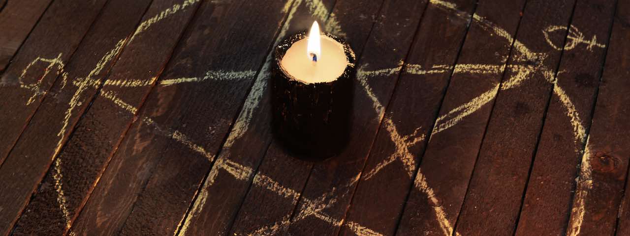 Eine brennende Kerze steht in der Mitte eines mit Kreide gezeichneten Pentagramm-Symbols.